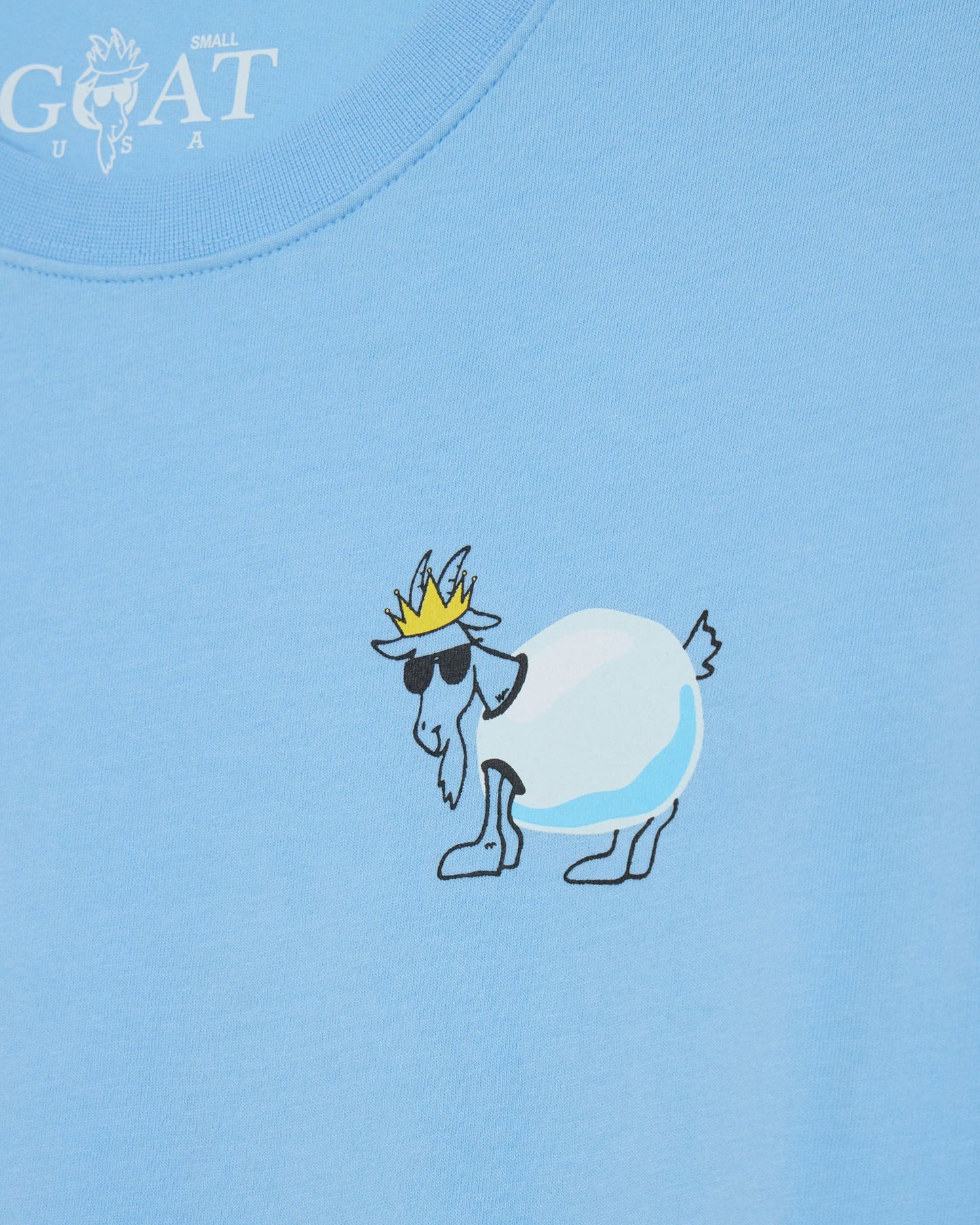 Light blue t-shirt with a cartoon goat wearing sunglasses and a crown on a light blue background.
