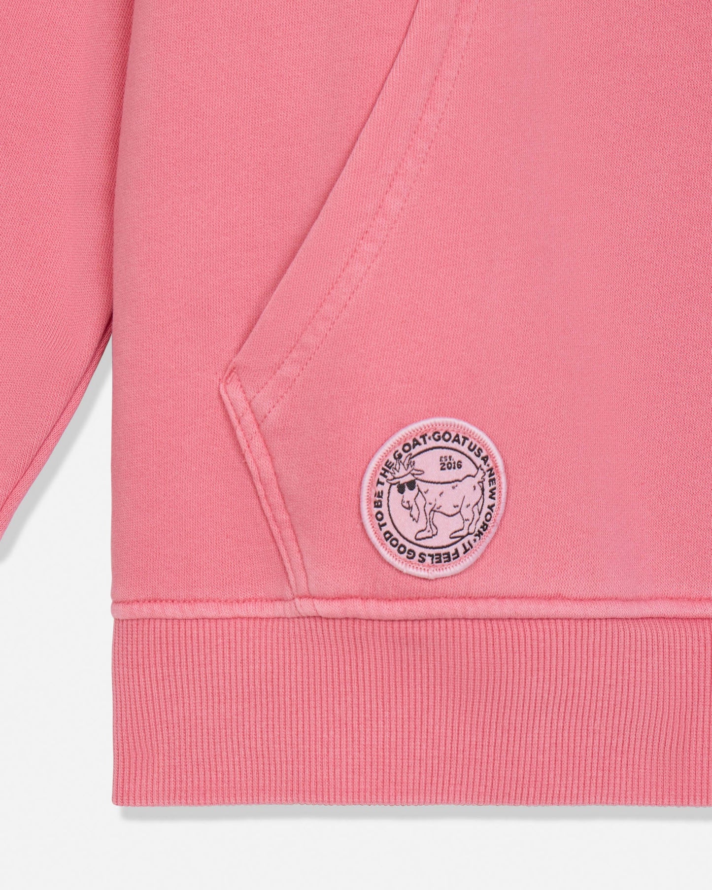 Close-up of a salmon-colored sweatshirt with a logo on the pocket against a white background