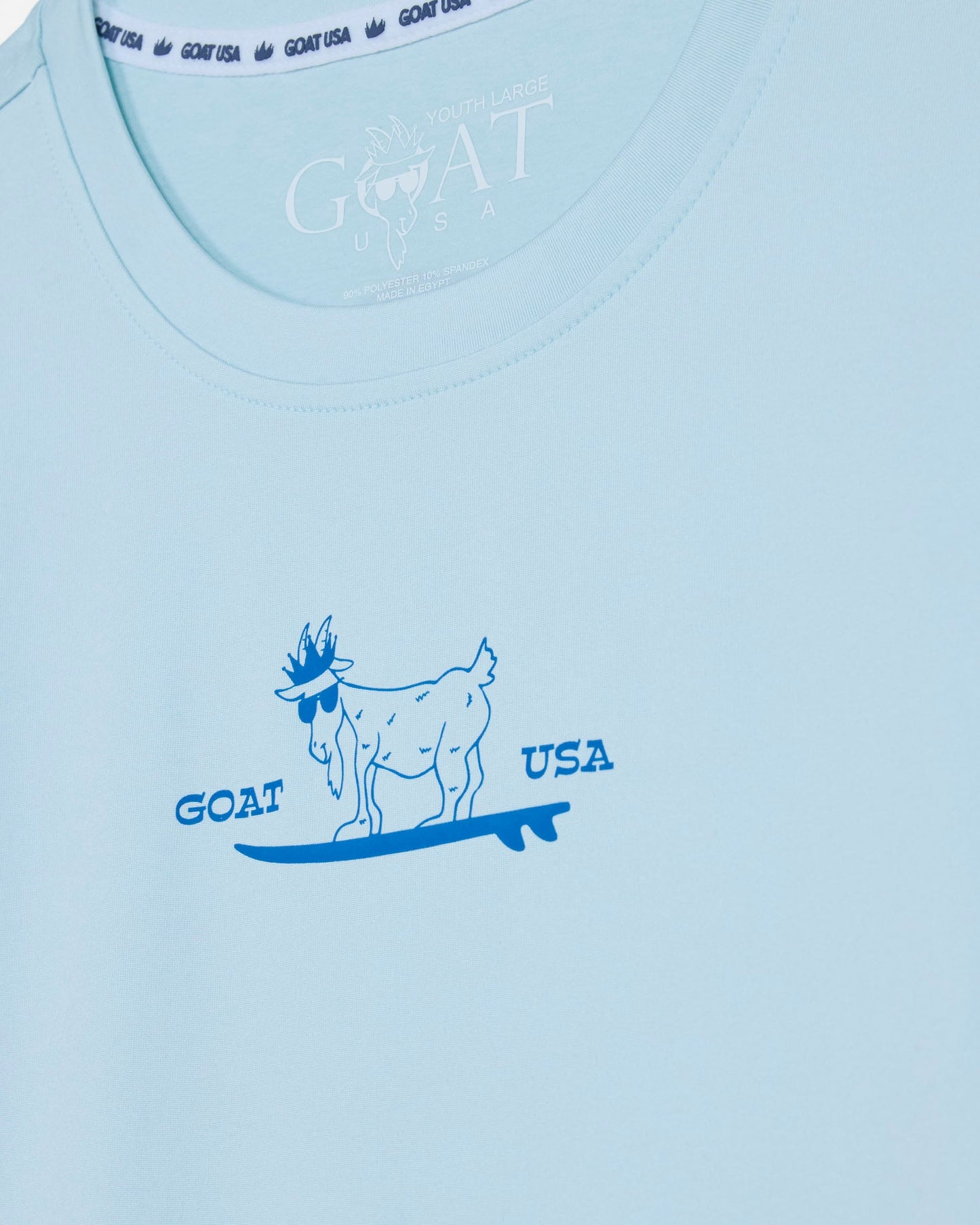 Light blue t-shirt with a graphic of a goat on a surfboard and 'GOAT USA' text.#color_delicate-blue