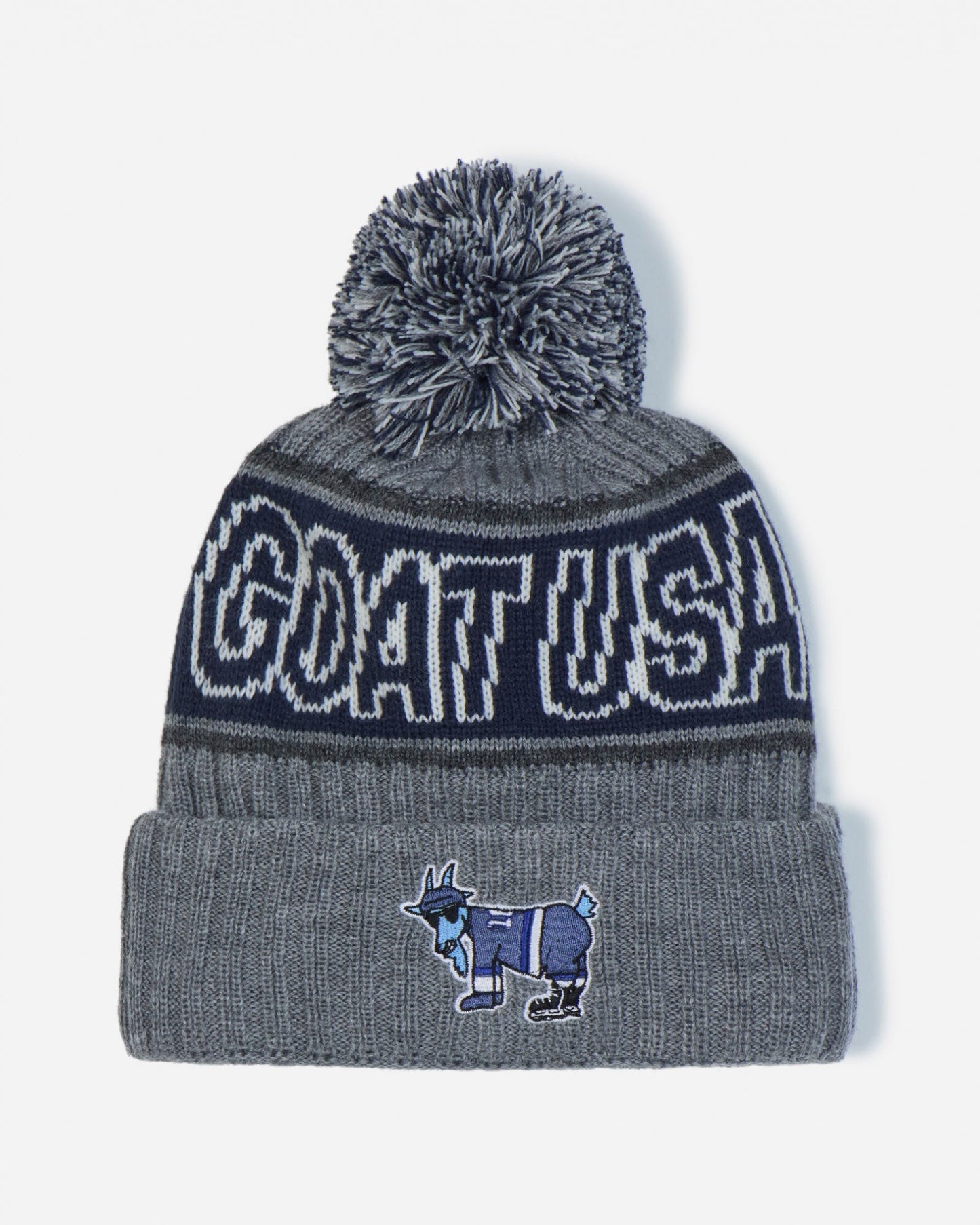 A gray and navy blue knit beanie with a gray pom-pom, featuring 'GOAT USA' in white lettering on a navy band and a small goat mascot patch on the front cuff.