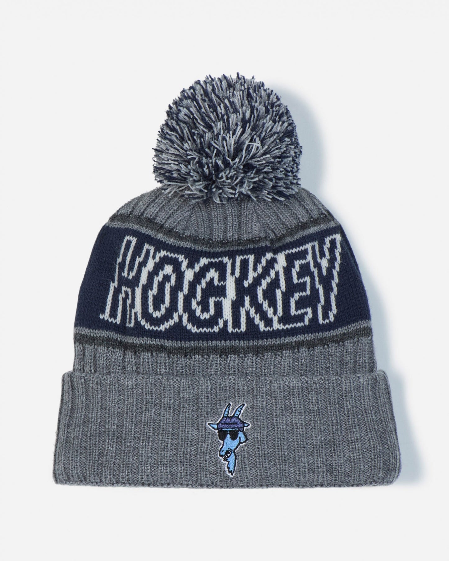 A gray and navy blue knit pom-pom beanie featuring the word 'HOCKEY' in white across the upper band and a small blue mascot logo on the front cuff.