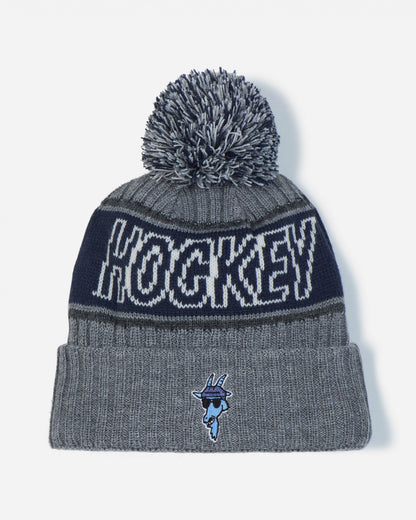 A gray and navy blue knit pom-pom beanie featuring the word 'HOCKEY' in white across the upper band and a small blue mascot logo on the front cuff.