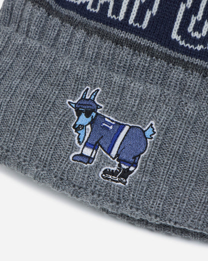 Close-up of a gray knit beanie with a blue embroidered goat mascot logo on the cuff, showing part of a navy and gray patterned band at the top.