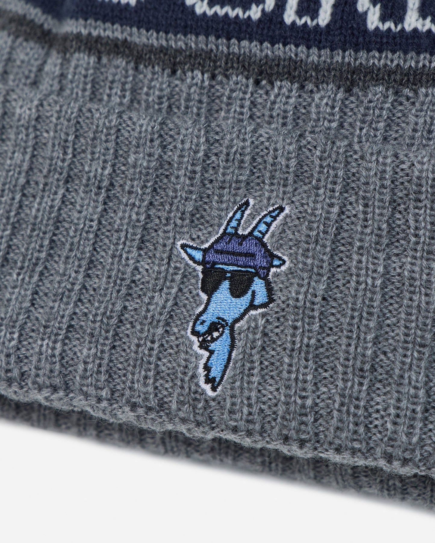 Close-up of a gray ribbed knit beanie with a blue embroidered goat mascot wearing sunglasses and a purple hat on the front cuff.