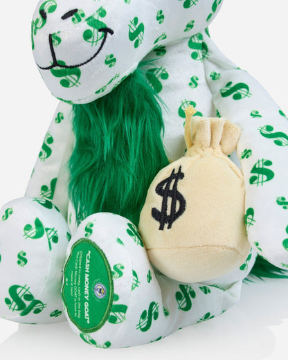 A plush goat toy in a white fabric printed with green dollar signs, featuring bright green faux fur around the neck and holding a small beige plush money bag with a black dollar sign.