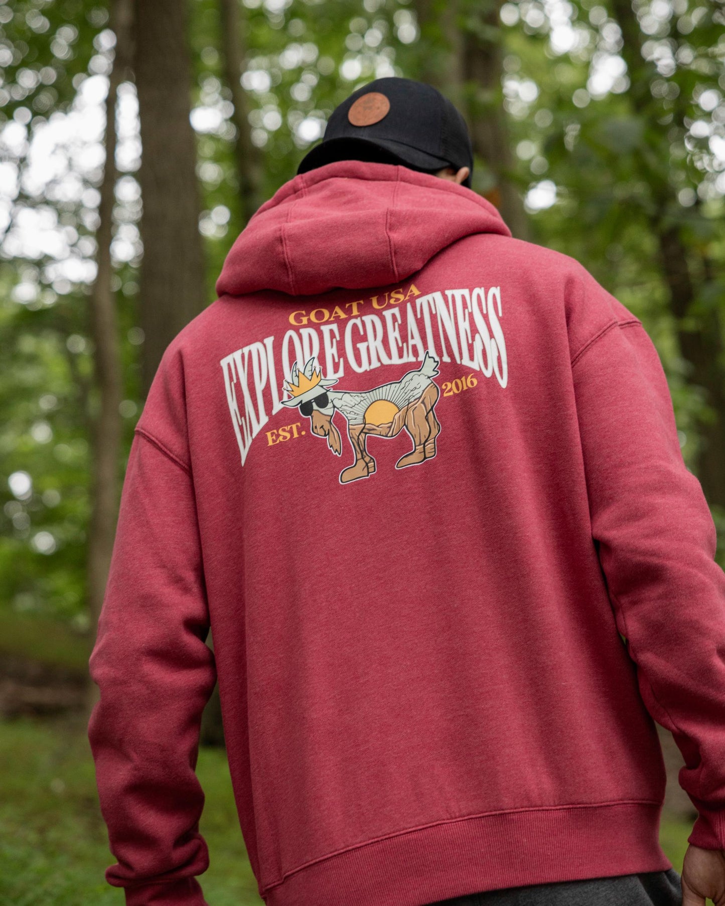 Person wearing a red hoodie with 'Explore Greatness' design outdoors#color_cardinal