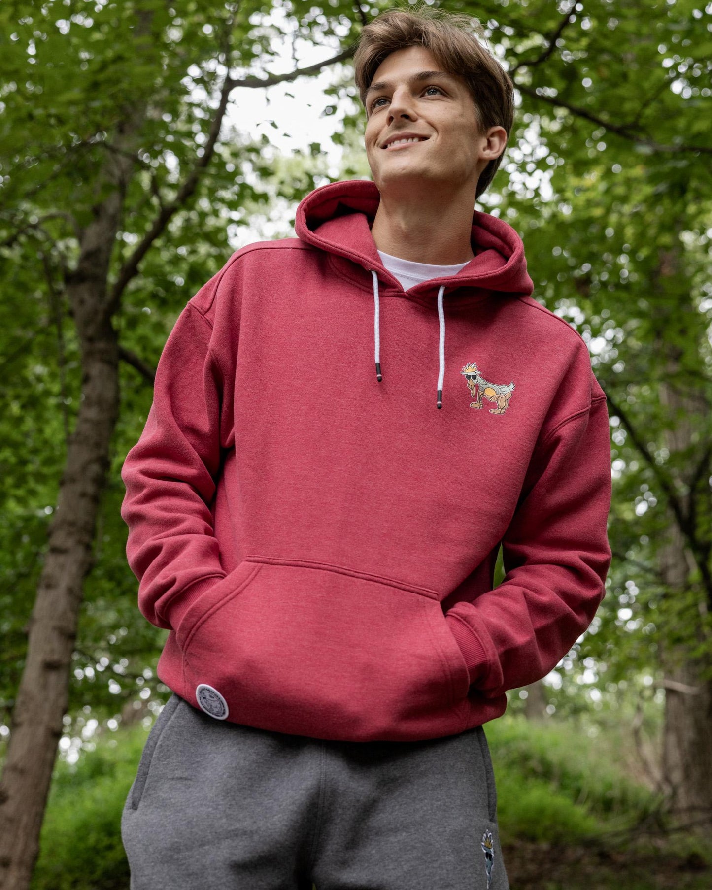 Person wearing a red hoodie with a small design, standing in a forest.#color_cardinal