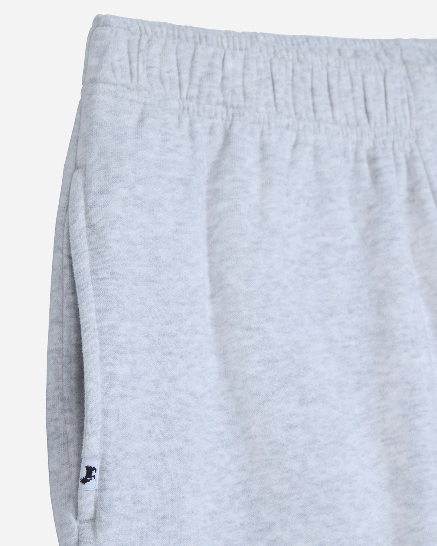 Close-up of light heather gray sweatpants showing the elastic waistband and side seam with a small black embroidered logo near the hem.#color_pale-gray-heather