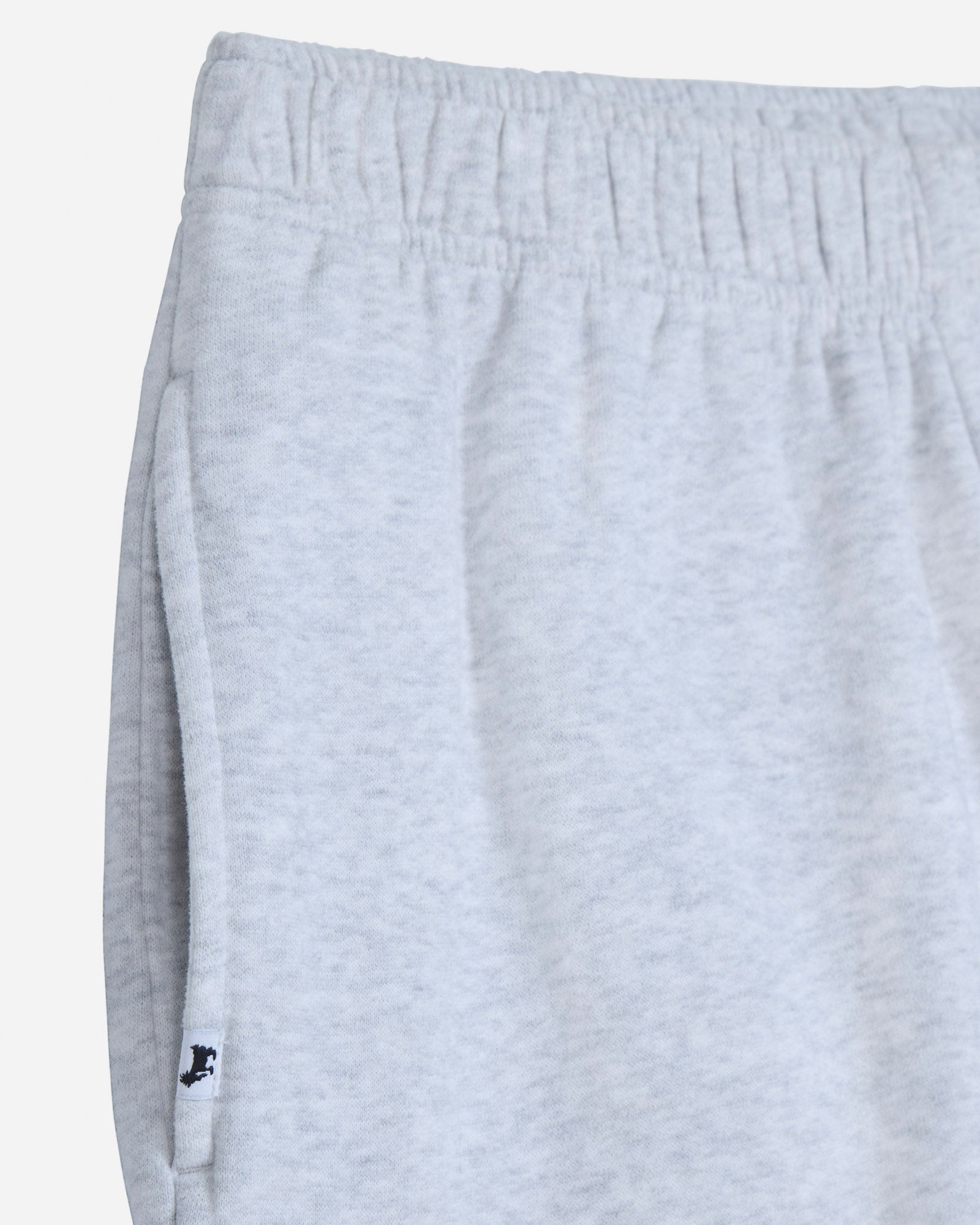 Close-up of light heather gray sweatpants showing the elastic waistband and side seam with a small black embroidered logo near the hem.#color_pale-gray-heather