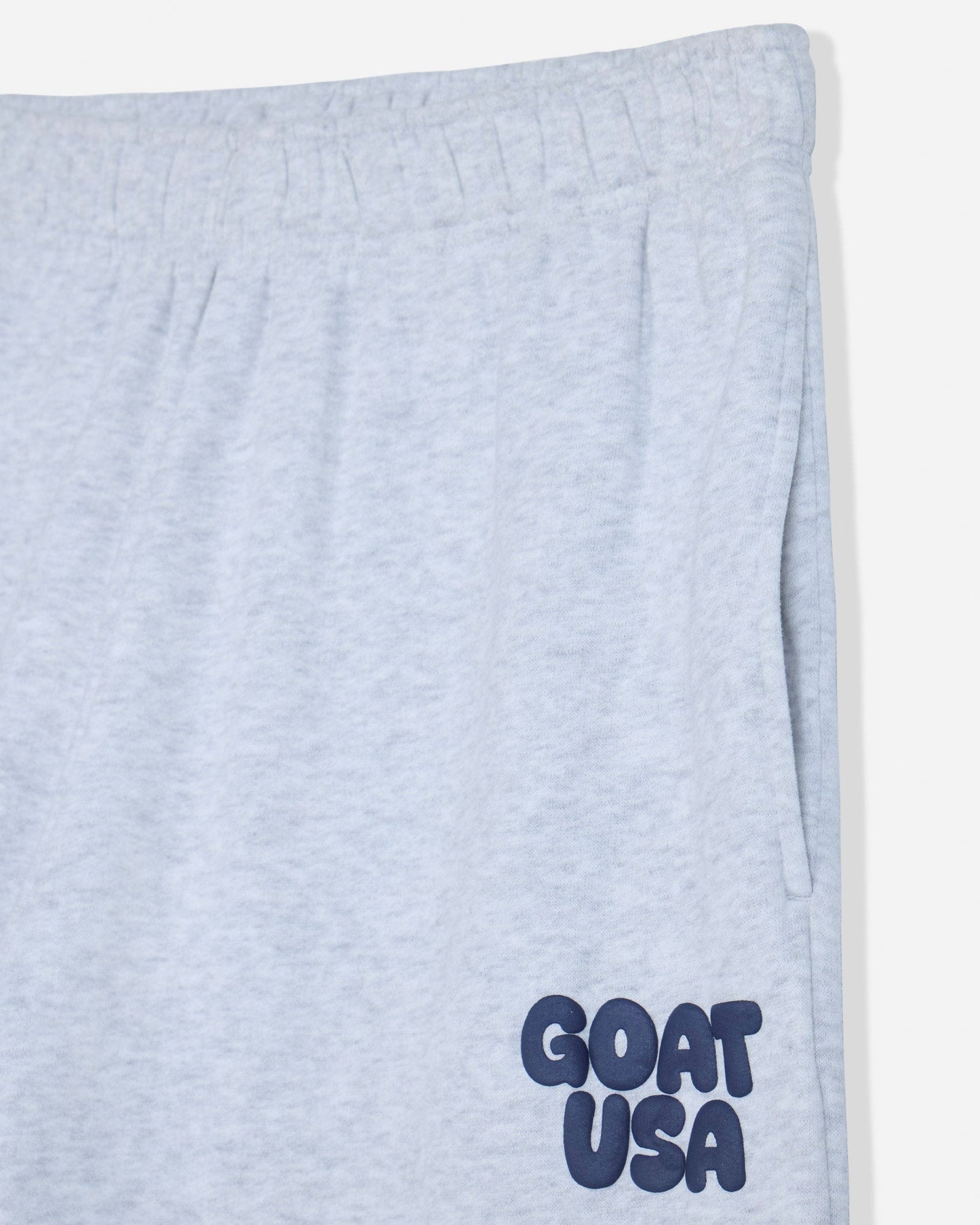 Close-up of light heather gray sweatpants with a navy blue 'GOAT USA' logo printed on the lower left leg.#color_pale-gray-heather
