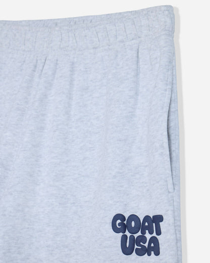 Close-up of light heather gray sweatpants with a navy blue 'GOAT USA' logo printed on the lower left leg.#color_pale-gray-heather