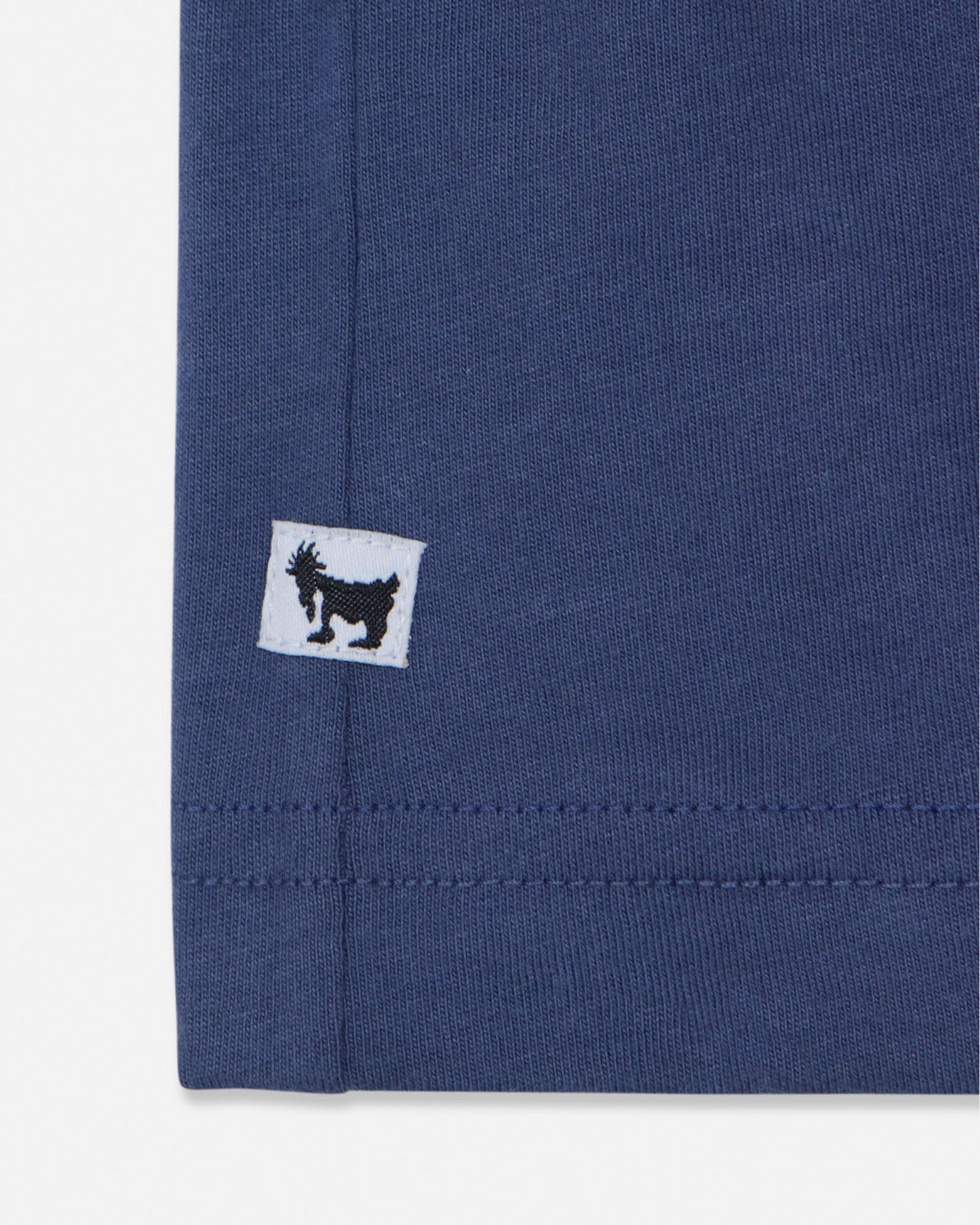 Close-up of a blue fabric with a small white label featuring a black logo on a white background#color_navy
