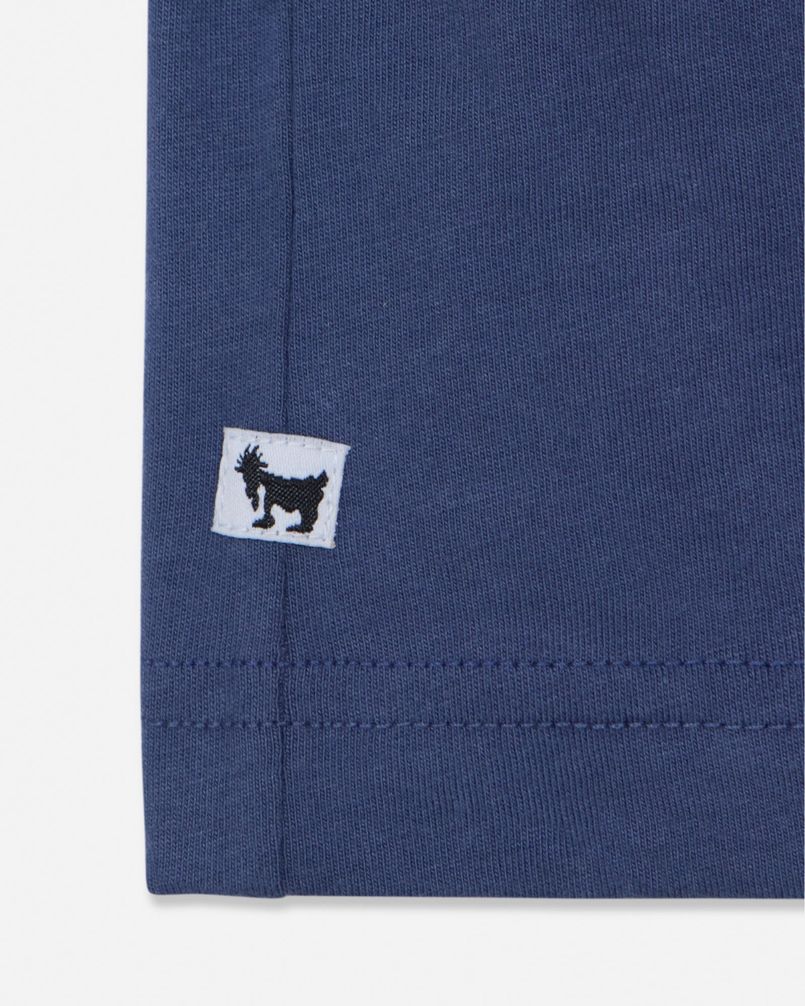 Close-up of a blue fabric with a small white label featuring a black logo on a white background#color_navy