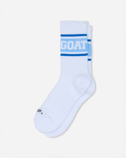 A pair of white crew socks with blue stripes and the word 'GOAT' printed in white on the front cuff, shown against a light gray background.#color_carolina-blue