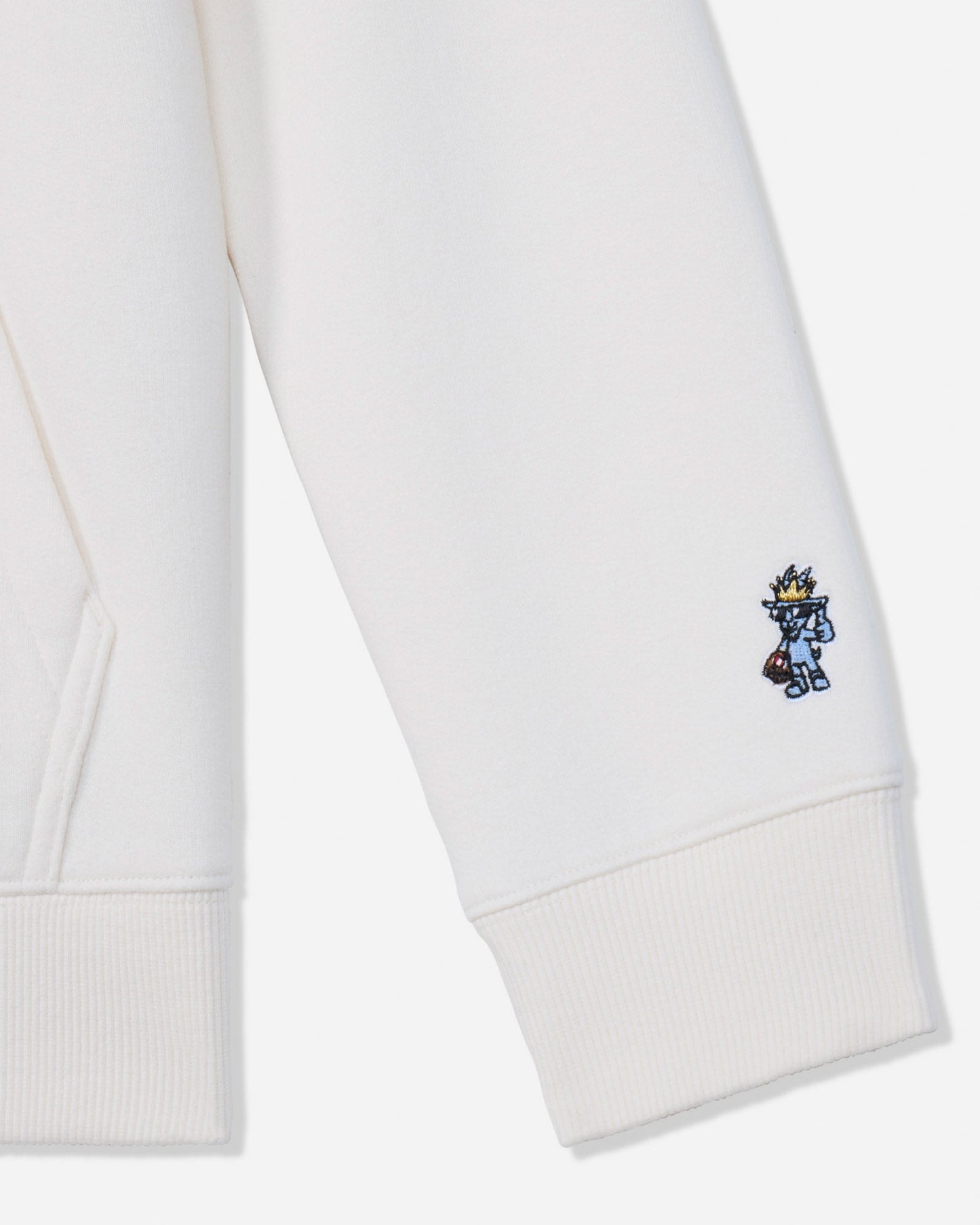 Close-up of a white ribbed cuff on a sweatshirt or hoodie, featuring a small embroidered blue and yellow character on the lower cuff.
