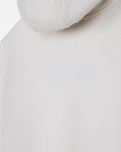 Close-up of a light off-white or cream-colored hoodie, showing the smooth fabric texture and the edge of the hood.