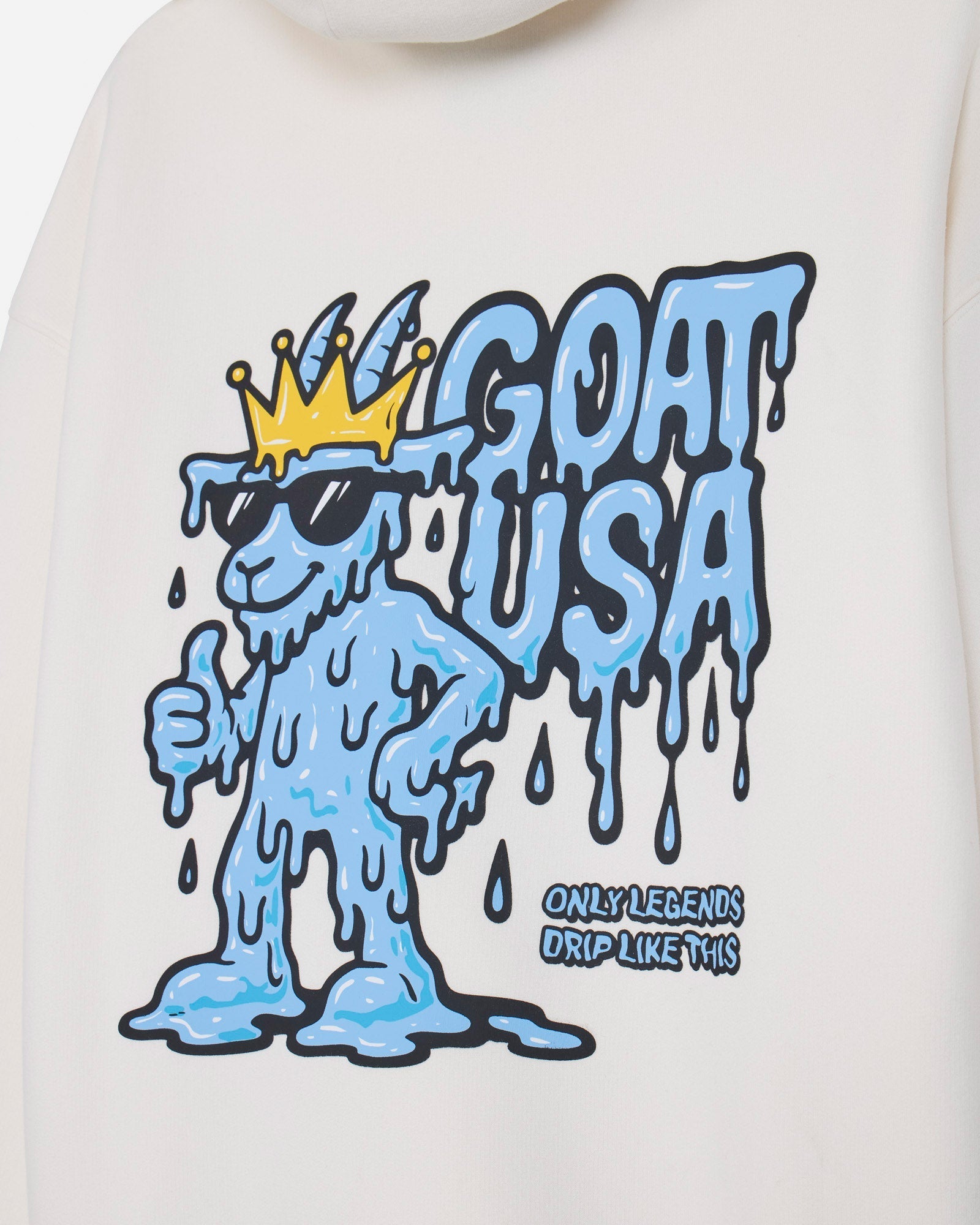 Close-up of a white sweatshirt featuring a blue and yellow melting cartoon character graphic with the text 'GOAT USA' and smaller text 'ONLY LEGENDS DRIP LIKE THIS'.