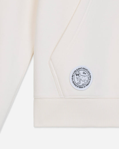 Close-up of a cream-colored sweatshirt showing the sleeve cuff, ribbed hem, and a circular embroidered patch on the chest.