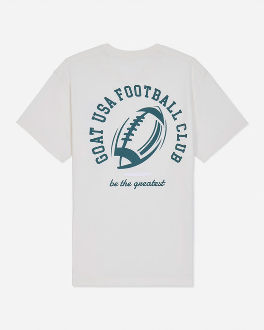 A white short-sleeve t-shirt with a dark green graphic on the front featuring an American football and the text 'GOAT USA FOOTBALL CLUB' and 'be the greatest'.