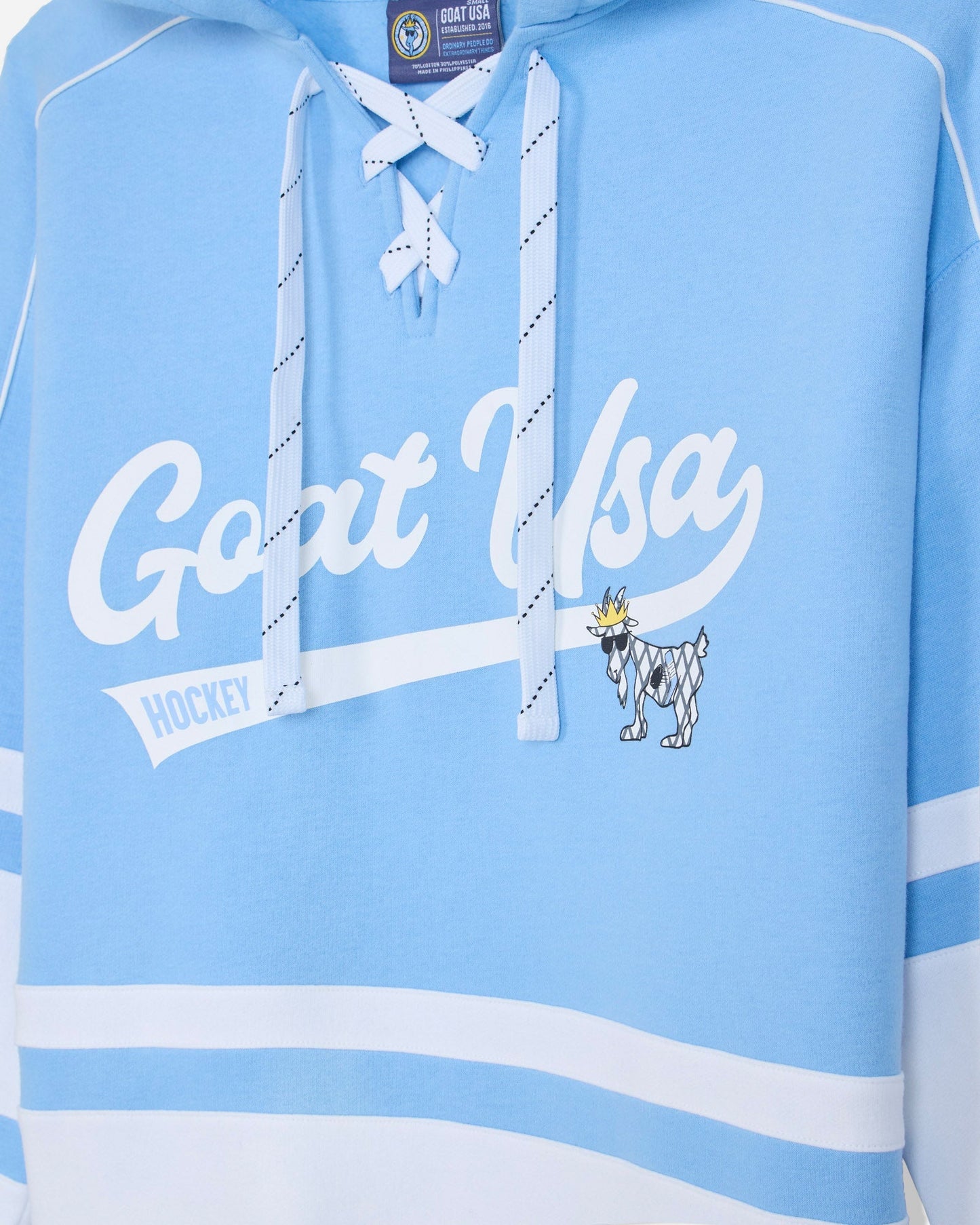 A light blue and white hooded sweatshirt featuring 'Goat USA HOCKEY' text across the chest, a small goat mascot graphic, and white drawstrings tied in a bow at the neckline.