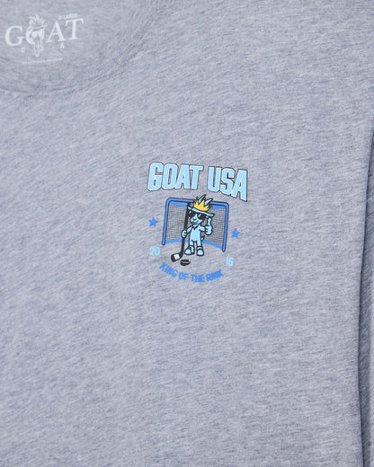 Close-up of a heather gray t-shirt featuring a 'GOAT USA' graphic on the chest with a cartoon hockey goat character and the text 'King of the Rink'.