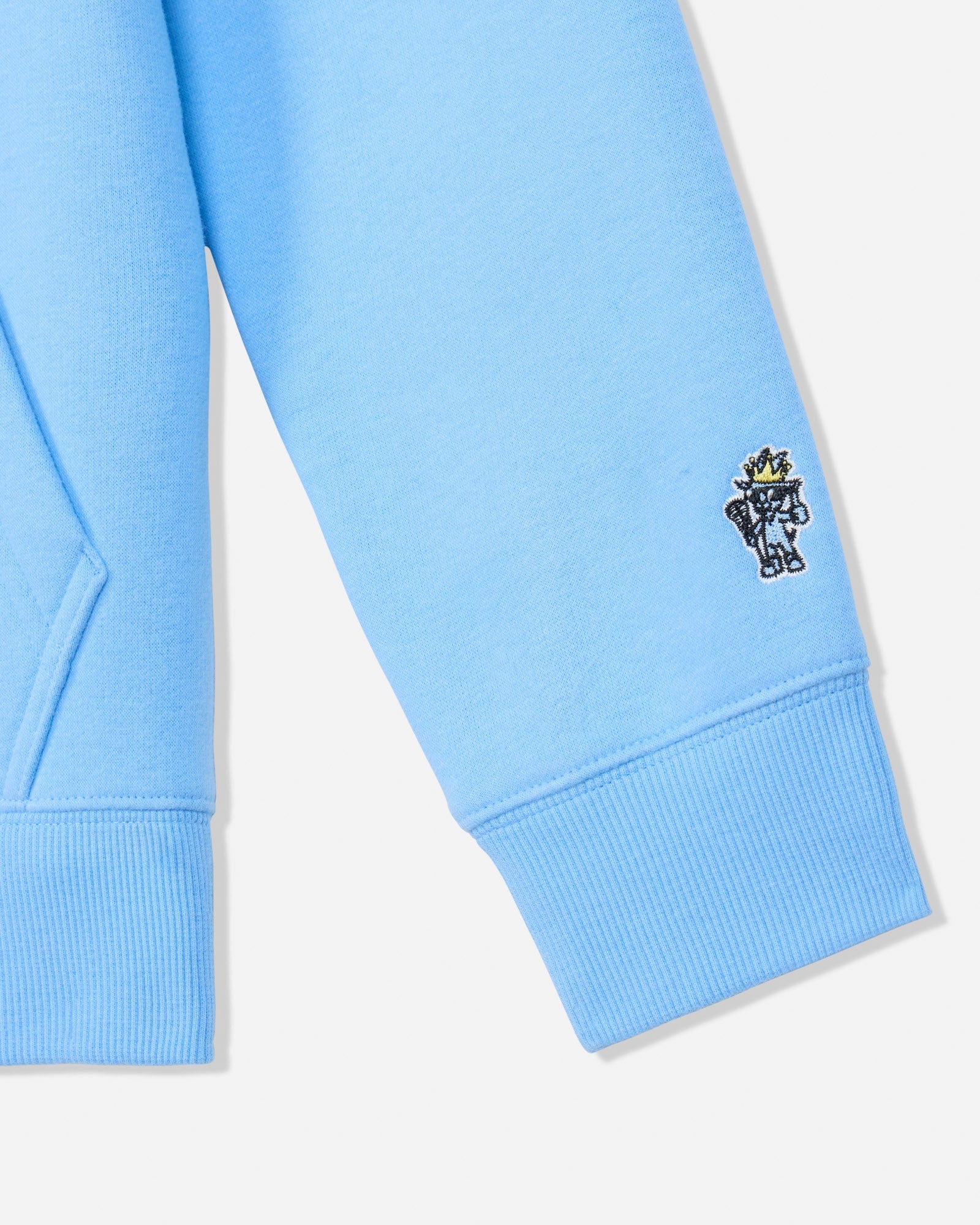 Close-up of a light blue sweatshirt sleeve with a small embroidered character patch on the cuff, shown against a plain light background.