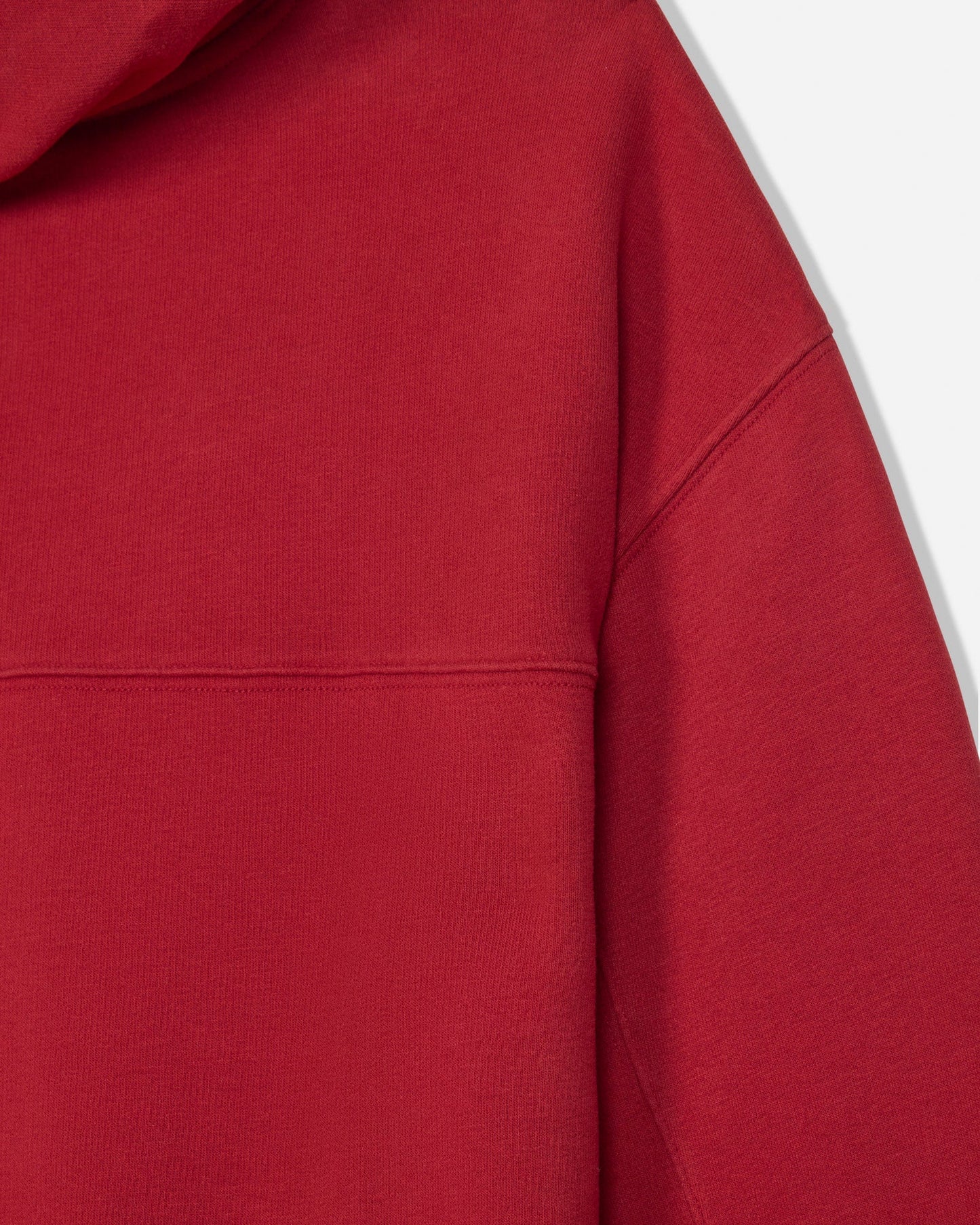Close-up of a red hooded sweatshirt showing the fabric texture, hood edge, and shoulder seam against a light gray background.