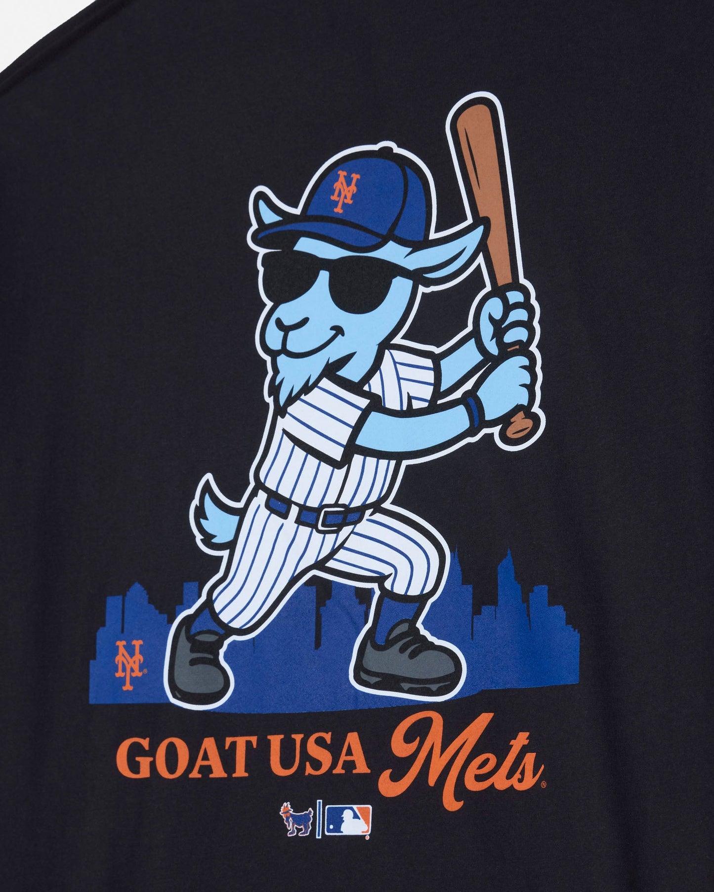 Close-up of a black graphic T-shirt featuring a cartoon goat baseball player in a blue and white pinstripe uniform, holding a bat, with 'GOAT USA Mets' text below.