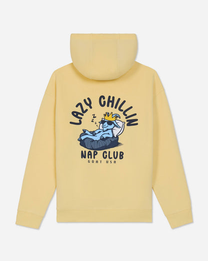 A pale yellow hooded sweatshirt shown from the back, featuring a large graphic print of a sleeping cartoon character on a bed with the text 'LAZY CHILLIN' and 'NAP CLUB' in black.