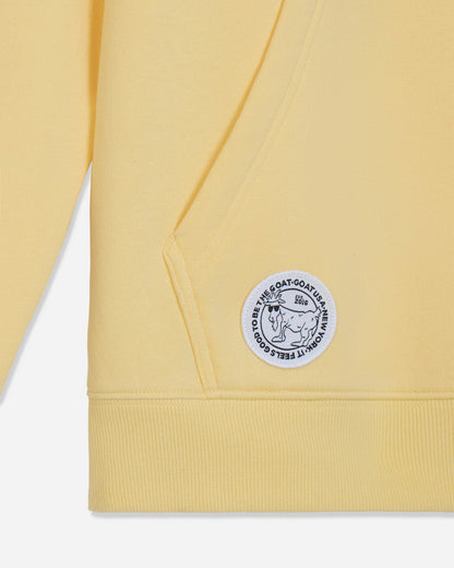 Close-up of a pale yellow sweatshirt showing the ribbed cuff, shoulder seam, and a circular white patch with black text and a goat illustration on the upper sleeve.