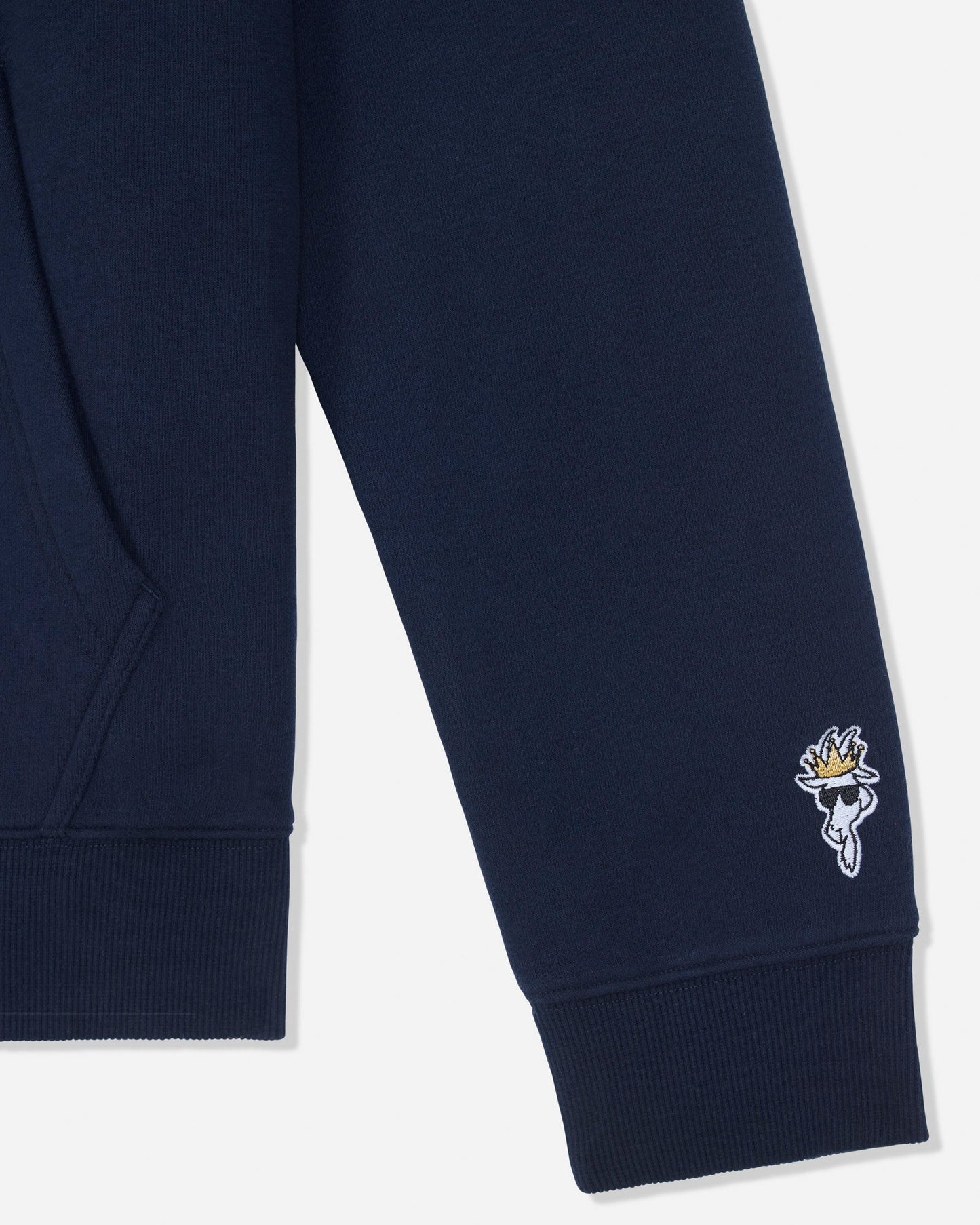 Close-up of a navy blue sweatshirt sleeve with a ribbed cuff and a small embroidered white and gold goat logo on the lower cuff, shown against a light gray background.#color_navy-blazer