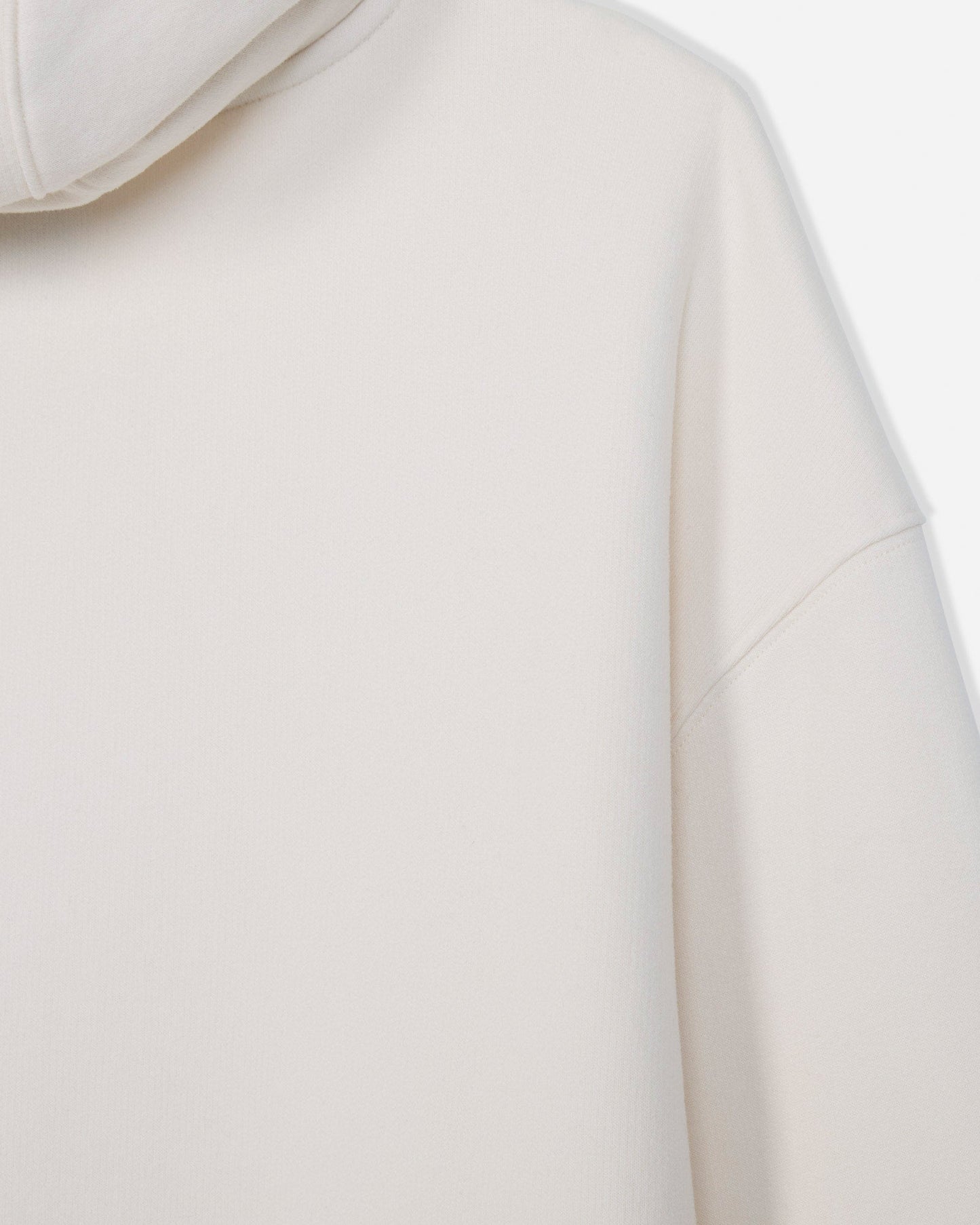 Close-up of a light cream or off-white hooded sweatshirt, showing the smooth fabric texture, hood edge, and shoulder seam against a very light neutral background.#color_bone
