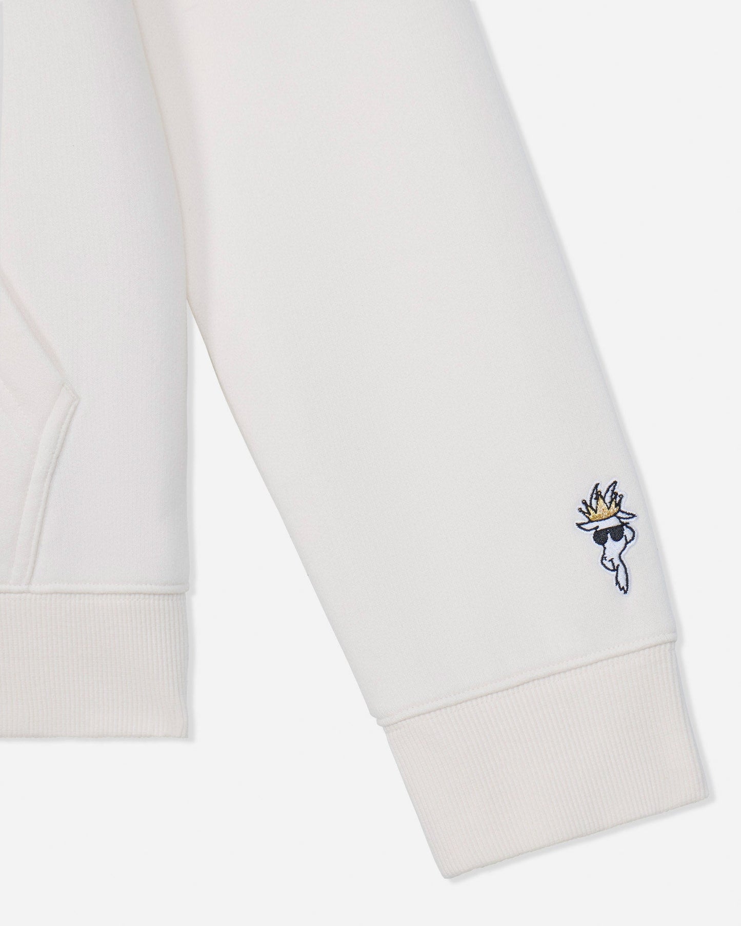 Close-up of a white sweatshirt sleeve with a small embroidered character logo featuring a gold flame and blue details on the cuff.#color_bone