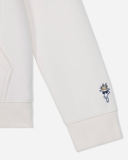 Close-up of a white sweatshirt sleeve with a small embroidered character logo featuring a gold flame and blue details on the cuff.#color_bone