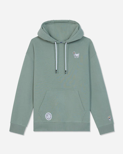 A sage green pullover hoodie with white drawstrings, featuring a small white goat graphic on the left chest and a circular patch on the lower left front pocket, displayed against a light gray background.#color_steeped-sage