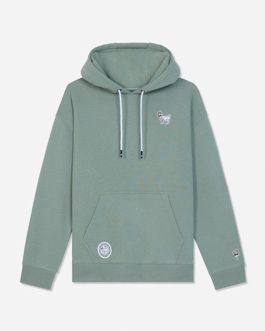 A sage green pullover hoodie with white drawstrings, featuring a small white goat graphic on the left chest and a circular patch on the lower left front pocket, displayed against a light gray background.#color_steeped-sage