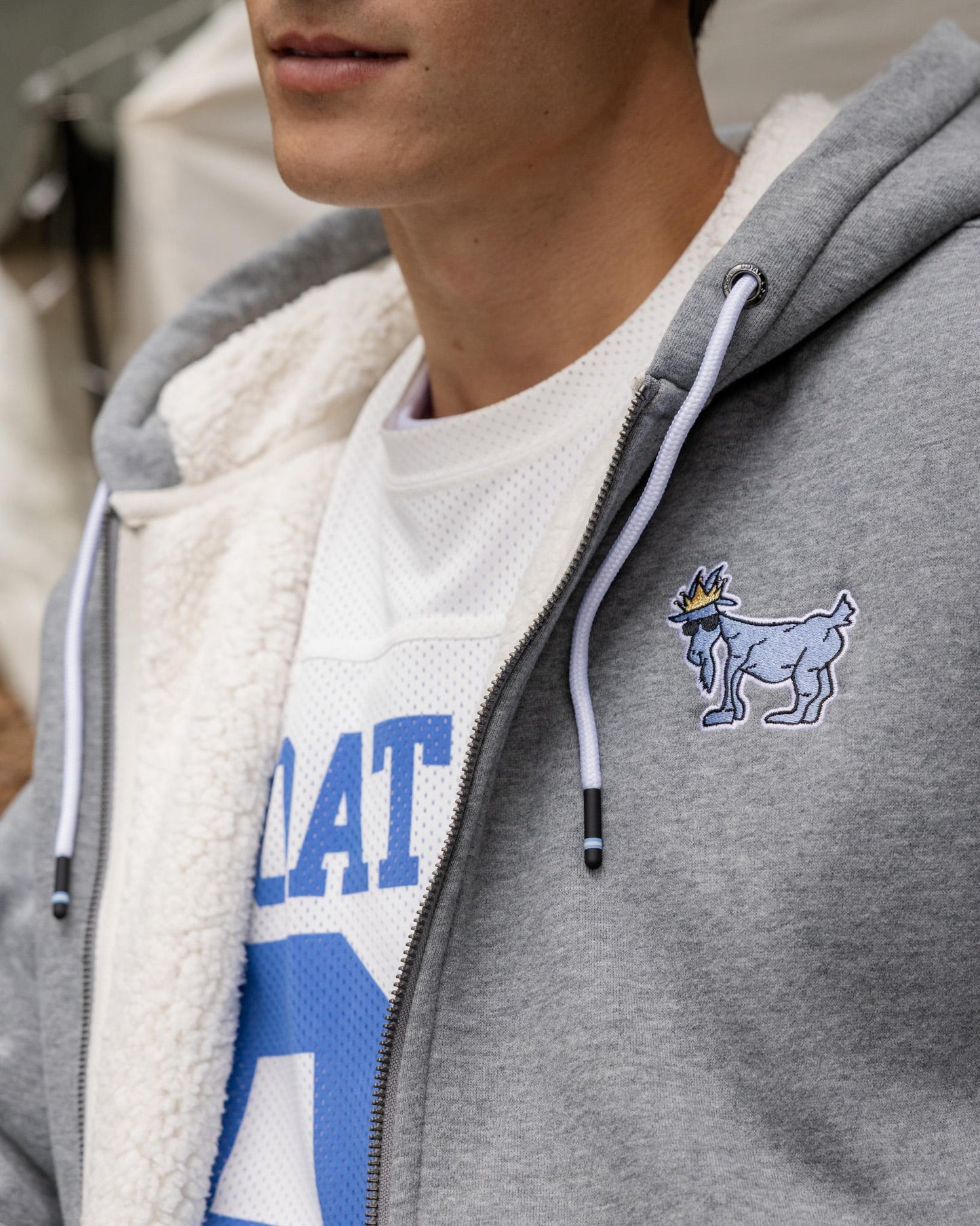 Person wearing a gray hoodie with a logo and a white shirt with blue text.#color_gray