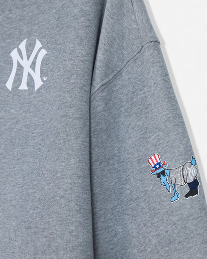 Close-up of a heather gray sweatshirt showing a white New York Yankees logo on the upper chest and a small multicolor graphic on the sleeve with a red, white, blue, and black design.