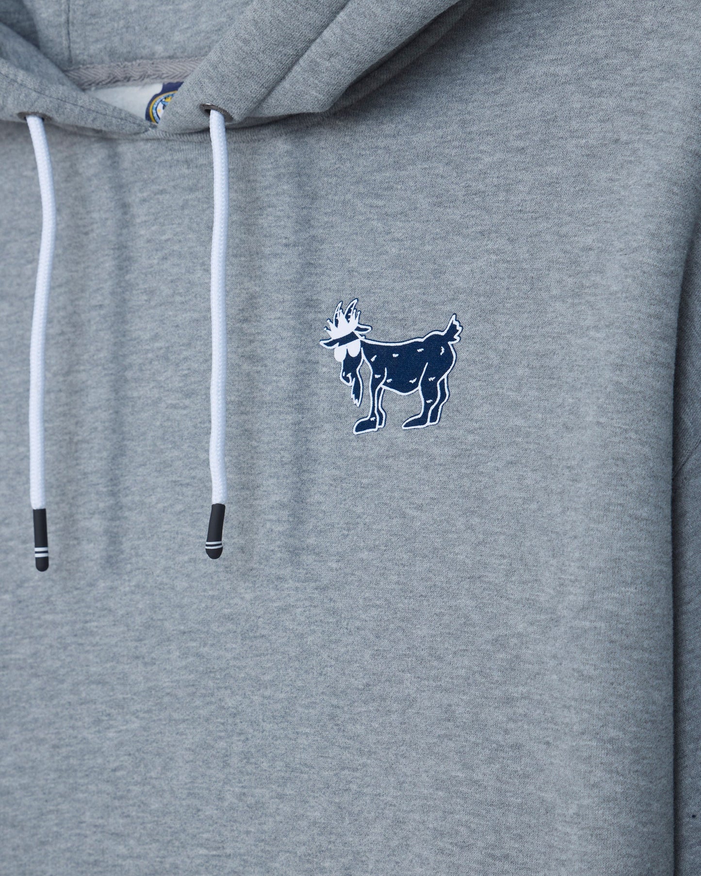 Close-up of a heather gray hoodie with white drawstrings and a small navy goat logo embroidered on the left chest.#color_gray