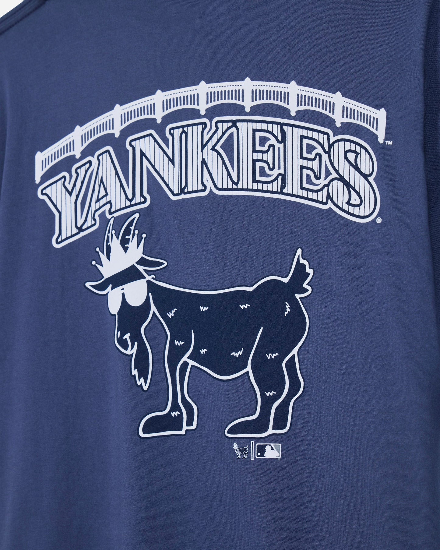 Close-up of a navy blue t-shirt featuring a white graphic of the New York Yankees logo, including the word 'YANKEES' in an arched font and a stylized goat mascot wearing sunglasses.#color_navy