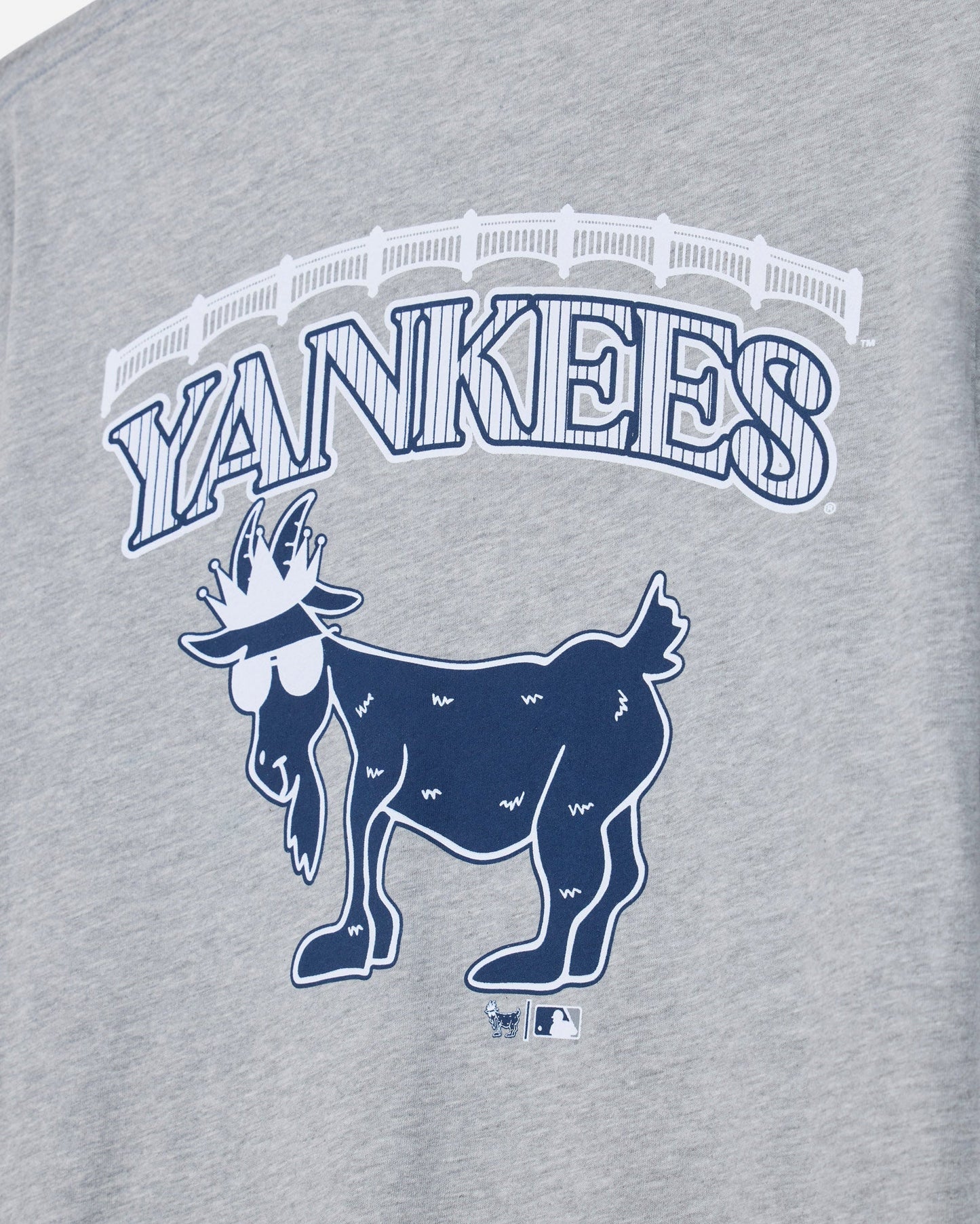 Close-up of a heather gray graphic T-shirt featuring the word 'YANKEES' in arched outlined letters above a navy blue goat logo, with a small MLB logo below.#color_gray