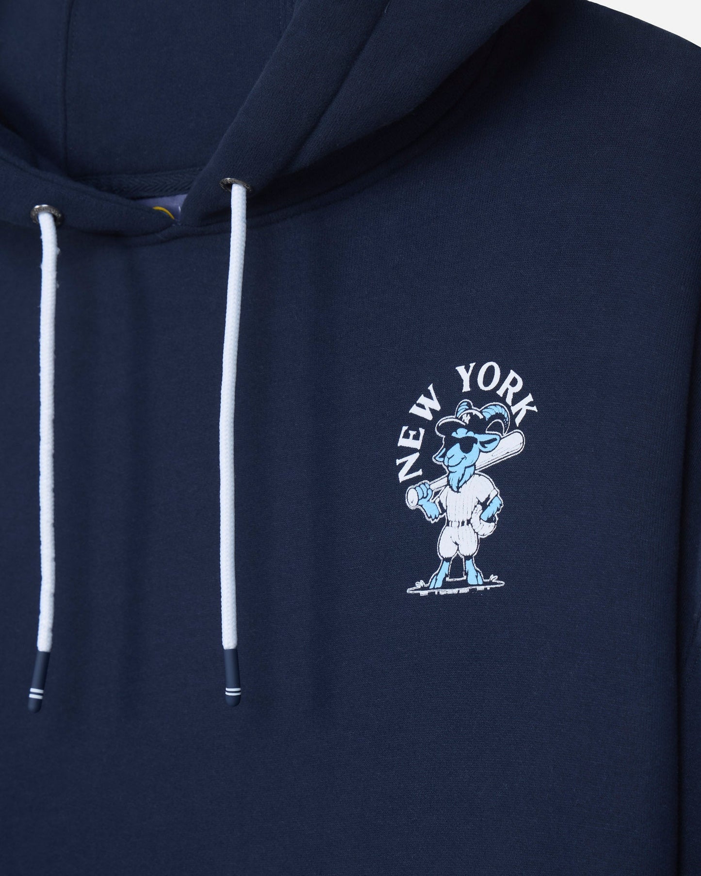 Close-up of a navy blue hoodie featuring white drawstrings and a light blue and white embroidered New York GOAT USA graphic on the left chest.