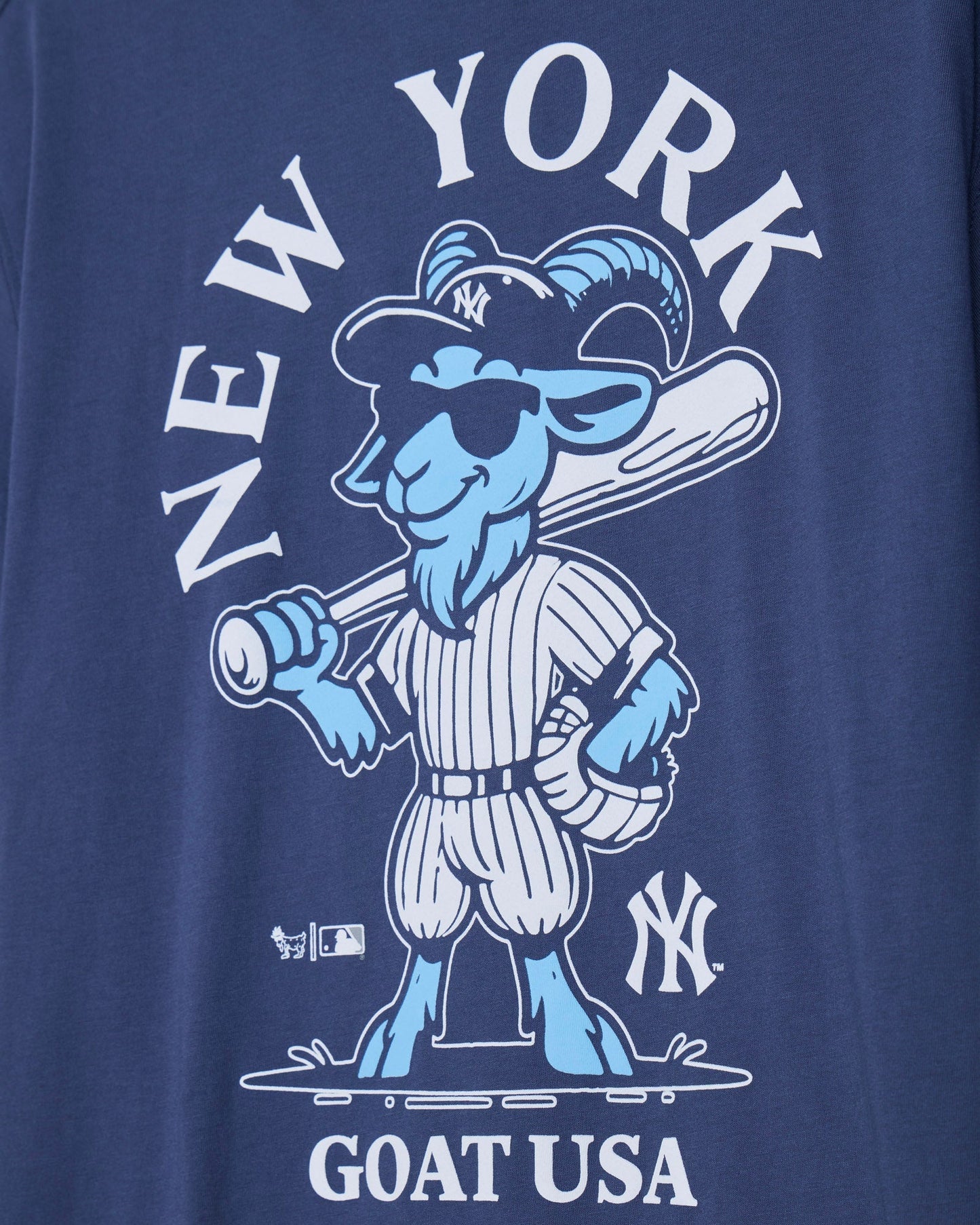 Close-up of a navy blue graphic t-shirt featuring a light blue and white cartoon goat baseball player with 'NEW YORK' above and 'GOAT USA' below.