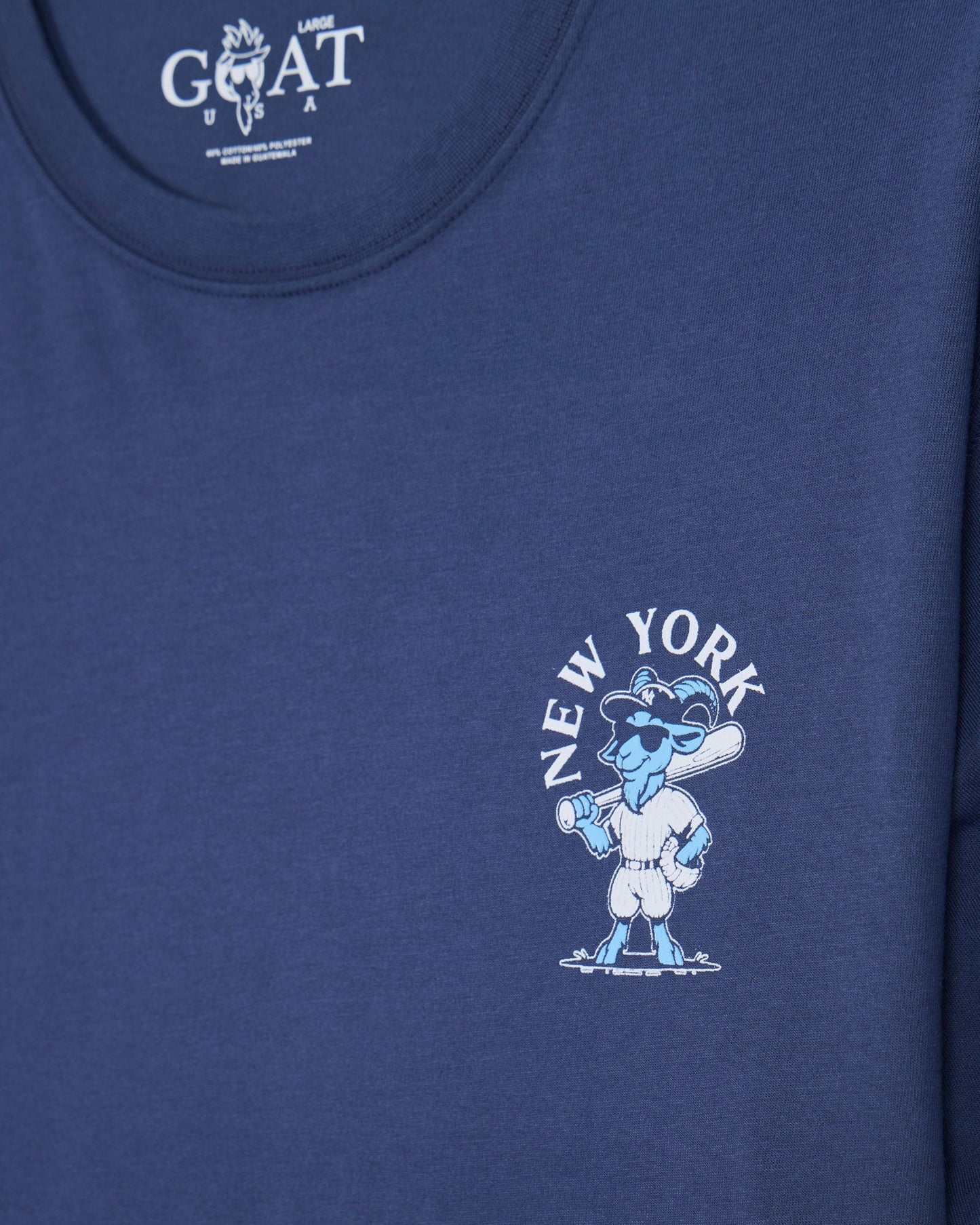 Close-up of a blue short-sleeve t-shirt featuring a light blue and white New York-themed cartoon graphic on the left chest with the text 'NEW YORK' arched above it.