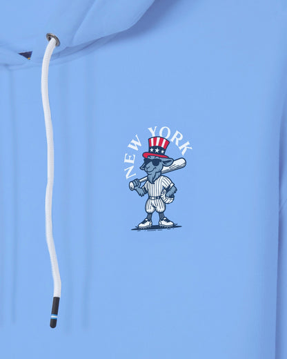 A close-up of a light blue hoodie featuring a cartoon New York baseball character wearing a red, white, and blue Uncle Sam hat, with the text 'NEW YORK' arched above it. A white drawstring is visible on the left side.#color_carolina-blue