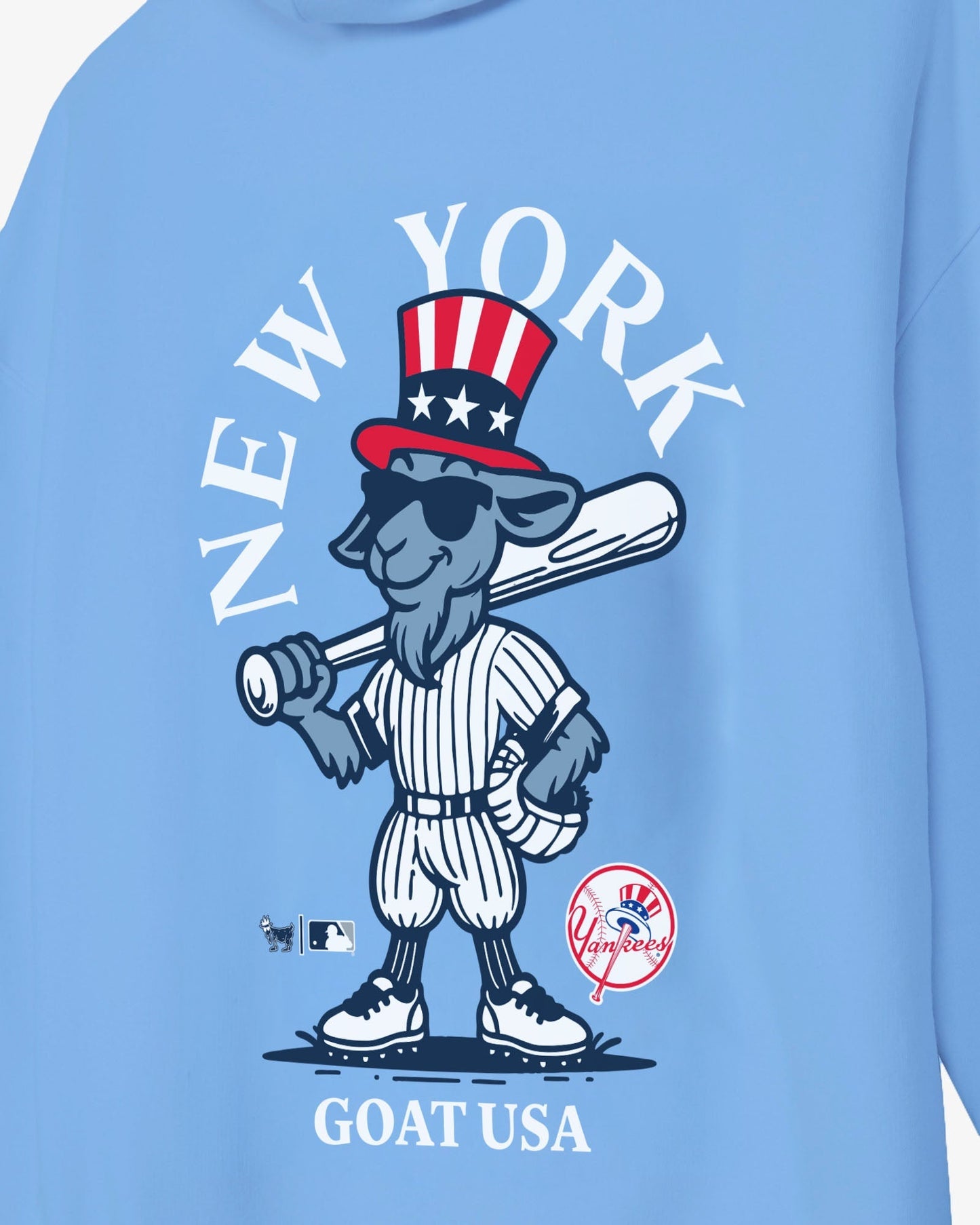 A close-up of a light blue sweatshirt featuring a cartoon goat baseball player wearing a red, white, and blue Uncle Sam hat, with the text 'NEW YORK' arched above and 'GOAT USA' below.#color_carolina-blue