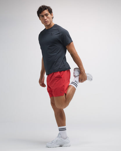 Man wearing a black t-shirt, red shorts, and white sneakers on a light gray background#color_poinsettia