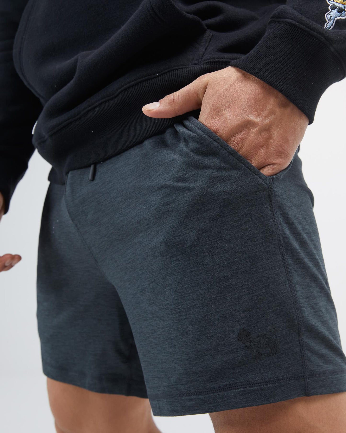 Person wearing dark gray shorts with a small logo on a light gray background#color_space-dye-black