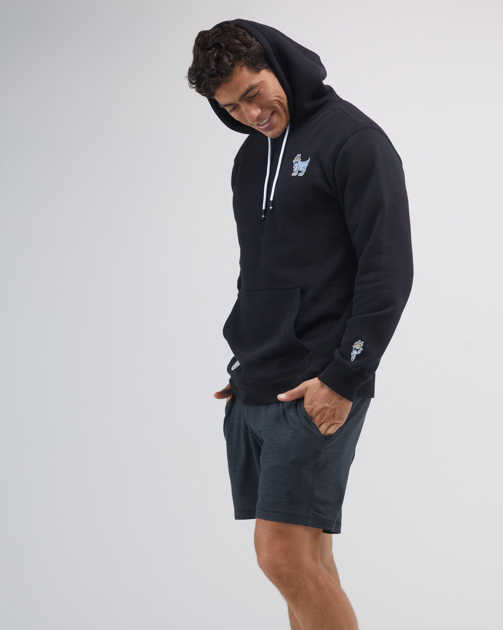 Person wearing a black hoodie and dark gray shorts on a white background#color_space-dye-black