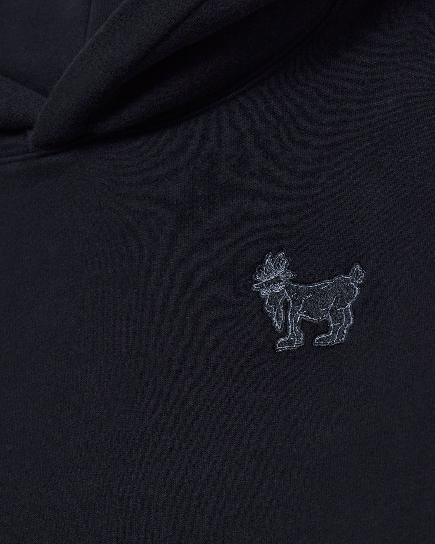 Black fabric with a small embroidered logo of a goat on a dark background#color_black